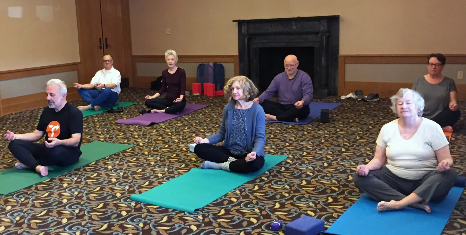 7 EPIC Members doing a seated yoga pose on yoga mats in a room