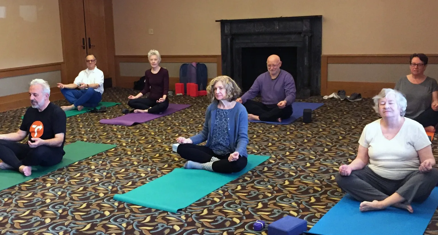 7 people doing a yoga pose in a sitting position on yoga mats